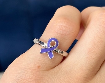 May include: A silver ring with a purple ribbon design. The ribbon is a symbol of awareness for various causes.