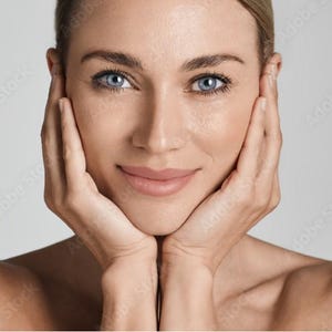 May include: A close-up portrait of a person with light skin and blue eyes. They are smiling and have their hands cupped around their face.