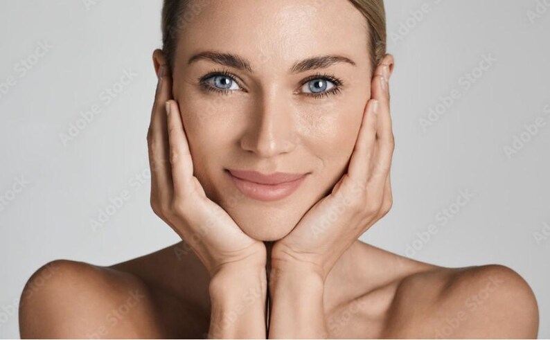 May include: A close-up portrait of a person with light skin and blue eyes. They are smiling and have their hands cupped around their face.