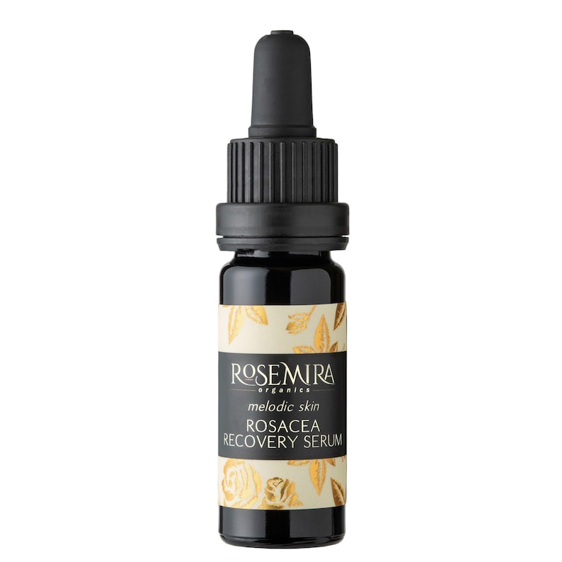 May include: A small, dark glass bottle with a black dropper top. The bottle is labeled "Rosemira Organics Melodic Skin Rosacea Recovery Serum" in gold lettering on a white background with a gold floral design.