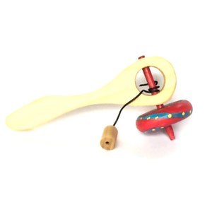 May include: A wooden toy top with a pull string and a handle. The top is red with blue and yellow accents. The handle and the pull string's base are light beige. The toy is designed for children.