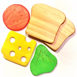May include: A set of five wooden toy food pieces, including a slice of cheese, a tomato, a piece of lettuce, and two slices of bread. The pieces are painted in bright colors and have a realistic appearance.