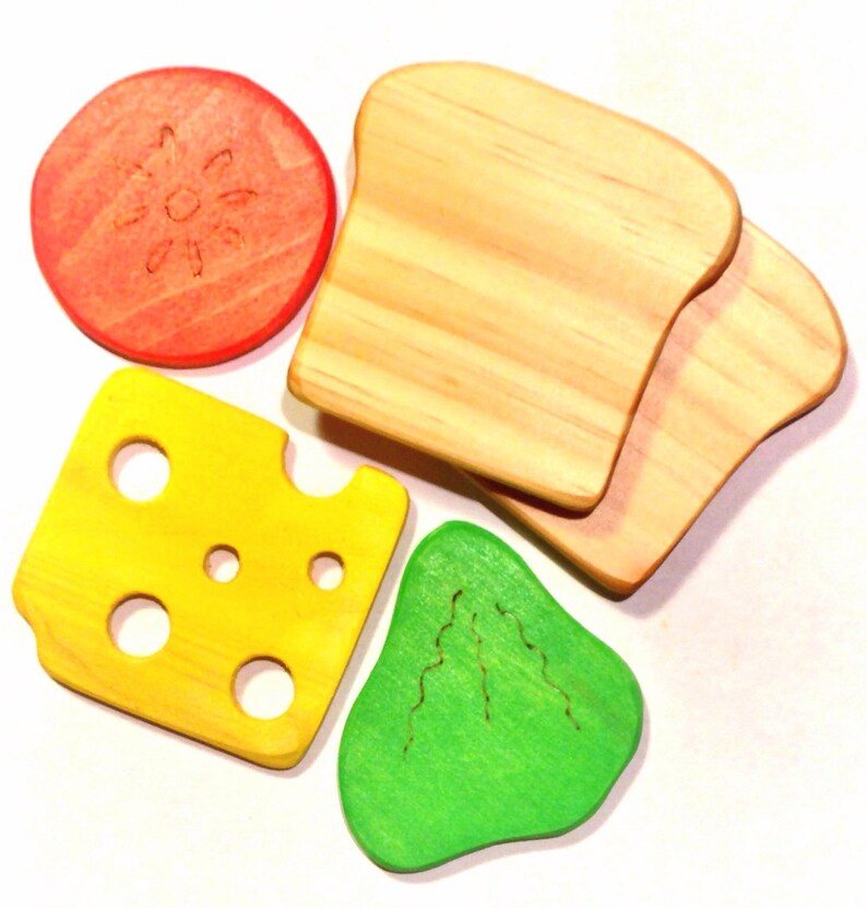 May include: A set of five wooden toy food pieces, including a slice of cheese, a tomato, a piece of lettuce, and two slices of bread. The pieces are painted in bright colors and have a realistic appearance.