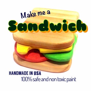May include: A wooden toy sandwich with yellow, red, and green pieces. The sandwich is made of wood and has a natural finish. The text "Make me a Sandwich" is printed on the top of the sandwich. The text "HANDMADE IN USA 100% safe and non toxic paint" is printed below the sandwich.