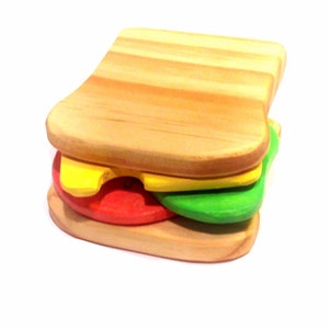 May include: A wooden toy sandwich with two slices of bread, a yellow cheese slice, a red tomato slice, and a green lettuce slice.