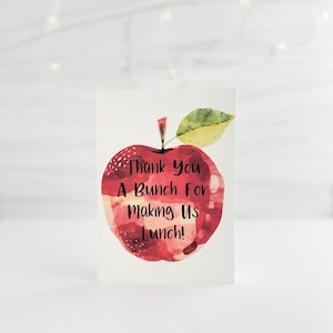 May include: A white card with a watercolor illustration of a red apple. The apple has a green leaf and the text "Thank You A Bunch For Making Us Lunch!" in black. The card is on a white background.