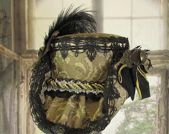 May include: A vintage-style hat in gold and black, featuring intricate lace, a feather, and decorative trim. The hat has a structured shape and a detailed design, with a bow and embellishments. The background shows a weathered window.