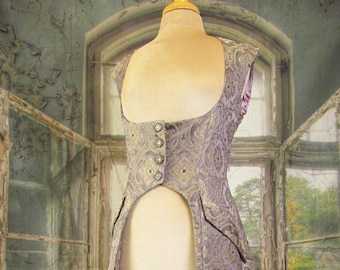 May include: A lavender and gold brocade vest with a high-low hemline, displayed on a mannequin. The vest features a decorative pattern, a button closure, and a satin lining. The garment is part of a historical or fantasy-themed costume.
