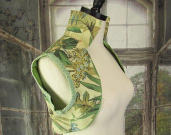 May include: A decorative, light green and floral patterned collar, displayed on a mannequin. The collar features a botanical design with green leaves and blue flowers. The edges are trimmed with a light green trim.