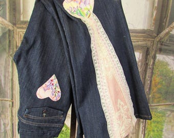 May include: Dark blue denim jeans with a decorative heart-shaped patch on the back pocket and another on the front. A wide strip of pink fabric with lace trim runs down the side. The jeans are hanging on a hanger.
