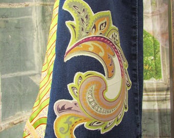 May include: Dark blue denim jeans with a colorful paisley design in shades of green, orange, and purple. The jeans have a decorative fabric panel on the side with green and white stripes.