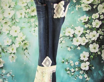 May include: Dark wash denim jeans with decorative lace and floral fabric accents. The jeans feature a lace patch on the back pocket and a flared bottom with lace trim and floral fabric inserts. The jeans are hanging on a wooden hanger.