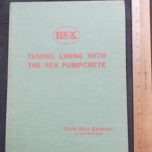May include: A light green book titled "Tunnel Lining with the Rex Pumpcrete" with red text and a red "REX" logo. The book is next to a wooden ruler with inch measurements.