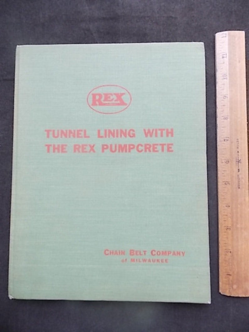 May include: A light green book titled "Tunnel Lining with the Rex Pumpcrete" with red text and a red "REX" logo. The book is next to a wooden ruler with inch measurements.
