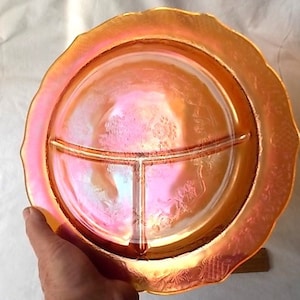 May include: An iridescent orange divided serving dish with a ruffled edge. The dish has three sections and a floral pattern. The dish is held by a hand.