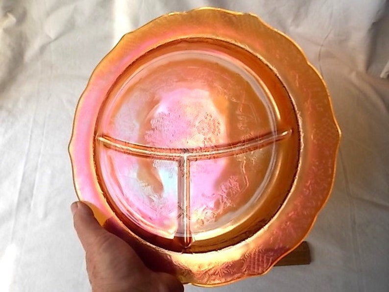 May include: An iridescent orange divided serving dish with a ruffled edge. The dish has three sections and a floral pattern. The dish is held by a hand.