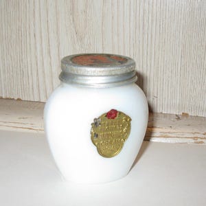 May include: A white, opaque glass jar with a silver lid and a gold label. The label has red and gold accents and text that reads "Sunshine Cream". The jar is likely an antique cosmetic container.