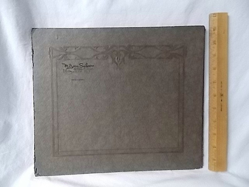 May include: A vintage gray photograph with decorative border and text from "M. Ben Salon, Dayton, Ohio". A wooden ruler, approximately 12 inches long, is positioned vertically next to the photograph.