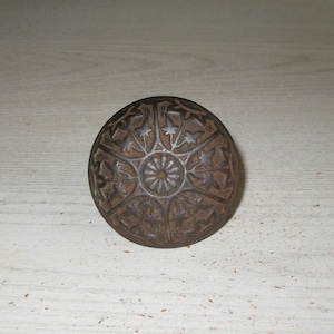 May include: A round, dark brown metal door knob featuring a raised, intricate floral pattern radiating from a central circular point. The surface displays a weathered, textured finish with detailed leaf and vine motifs embossed across the entire face.