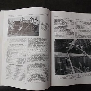 May include: An open book with black and white photographs and text. The left page features a photo of a construction site with a ladder. The right page shows a photo of a wooden structure. The book is open on a dark surface.