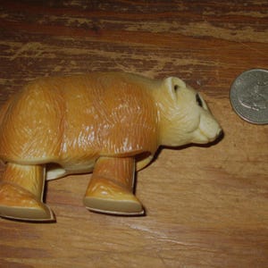 Peut inclure: Figurine d'ours brun clair avec une finition brillante. L'ours est &agrave; quatre pattes, avec une pi&egrave;ce de monnaie &agrave; c&ocirc;t&eacute; pour la comparaison de taille. La figurine est faite d'un mat&eacute;riau dur et a un design d&eacute;taill&eacute;.