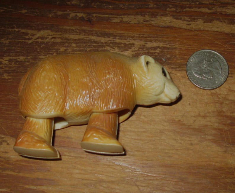 Peut inclure: Figurine d'ours brun clair avec une finition brillante. L'ours est &agrave; quatre pattes, avec une pi&egrave;ce de monnaie &agrave; c&ocirc;t&eacute; pour la comparaison de taille. La figurine est faite d'un mat&eacute;riau dur et a un design d&eacute;taill&eacute;.