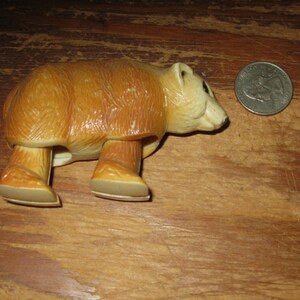 Peut inclure: Figurine de jouet ours vintage, marron et beige, avec une pi&egrave;ce de monnaie &agrave; c&ocirc;t&eacute; pour comparaison de taille. L'ours a une texture de fourrure d&eacute;taill&eacute;e et est pos&eacute; sur ses quatre pattes.
