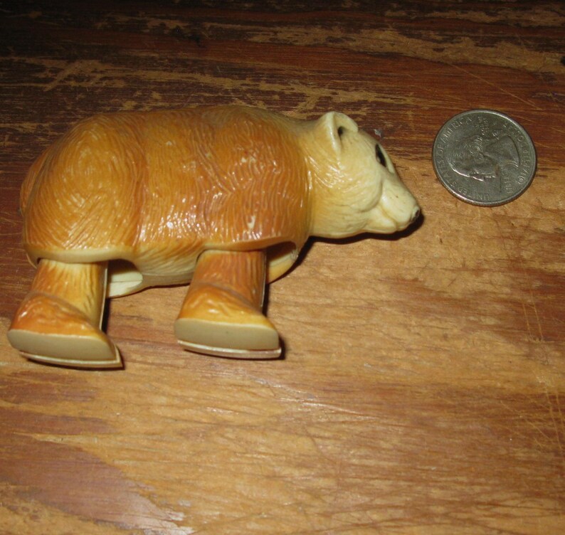 Peut inclure: Figurine de jouet ours vintage, marron et beige, avec une pi&egrave;ce de monnaie &agrave; c&ocirc;t&eacute; pour comparaison de taille. L'ours a une texture de fourrure d&eacute;taill&eacute;e et est pos&eacute; sur ses quatre pattes.