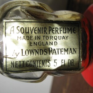 K&ouml;nnte beinhalten: Nahaufnahme einer Vintage-Parf&uuml;mflasche mit goldenem Etikett. Auf dem Etikett steht "A Souvenir Perfume, Made in Torquay England by Lownds Rateman, Nett Contents 5 Fl. Dr."
