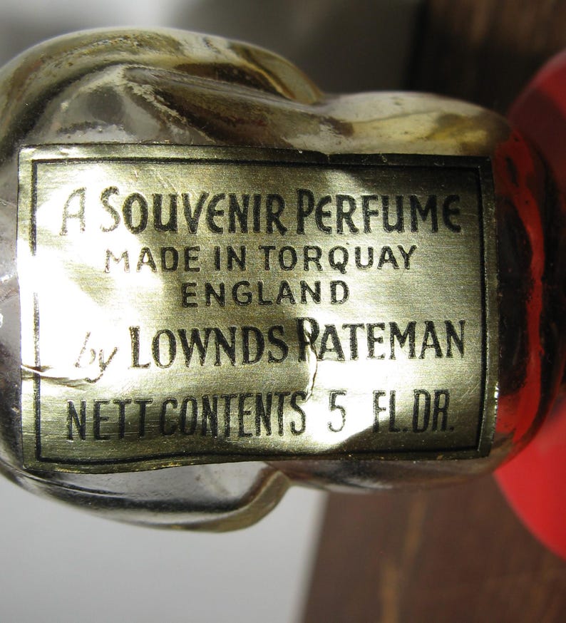 K&ouml;nnte beinhalten: Nahaufnahme einer Vintage-Parf&uuml;mflasche mit goldenem Etikett. Auf dem Etikett steht "A Souvenir Perfume, Made in Torquay England by Lownds Rateman, Nett Contents 5 Fl. Dr."