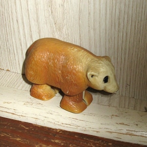 Peut inclure: Figurine d'ours de couleur beige clair avec une t&ecirc;te beige clair et des yeux fonc&eacute;s. L'ours est en position de marche, avec ses quatre pattes visibles. La figurine est en mat&eacute;riau brillant et repose sur une surface blanche et marron.