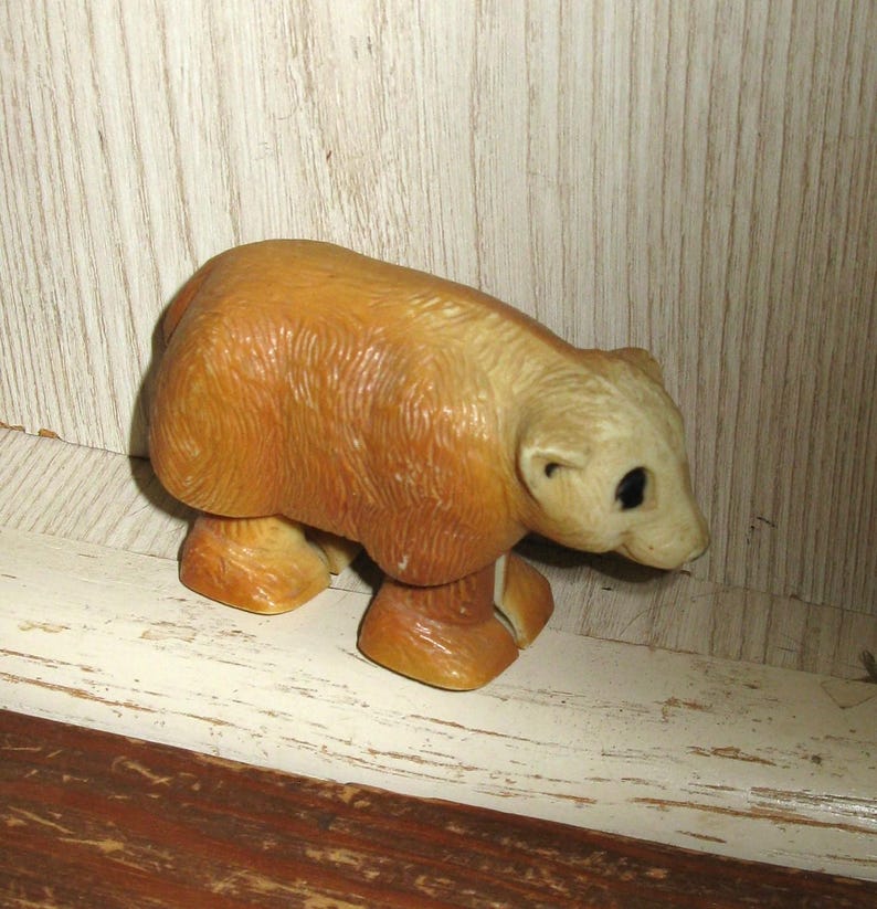 Peut inclure: Figurine d'ours de couleur beige clair avec une t&ecirc;te beige clair et des yeux fonc&eacute;s. L'ours est en position de marche, avec ses quatre pattes visibles. La figurine est en mat&eacute;riau brillant et repose sur une surface blanche et marron.