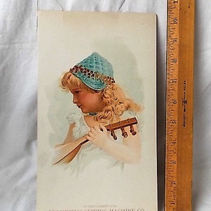 Może przedstawiać: Zabytkowa reklama drukowana dla "Domestic" Sewing Machine Co. przedstawiająca młodą dziewczynę z blond włosami w niebieskim berecie i trzymającą mały instrument strunowy. Drewniana linijka jest umieszczona po prawej stronie nadruku.