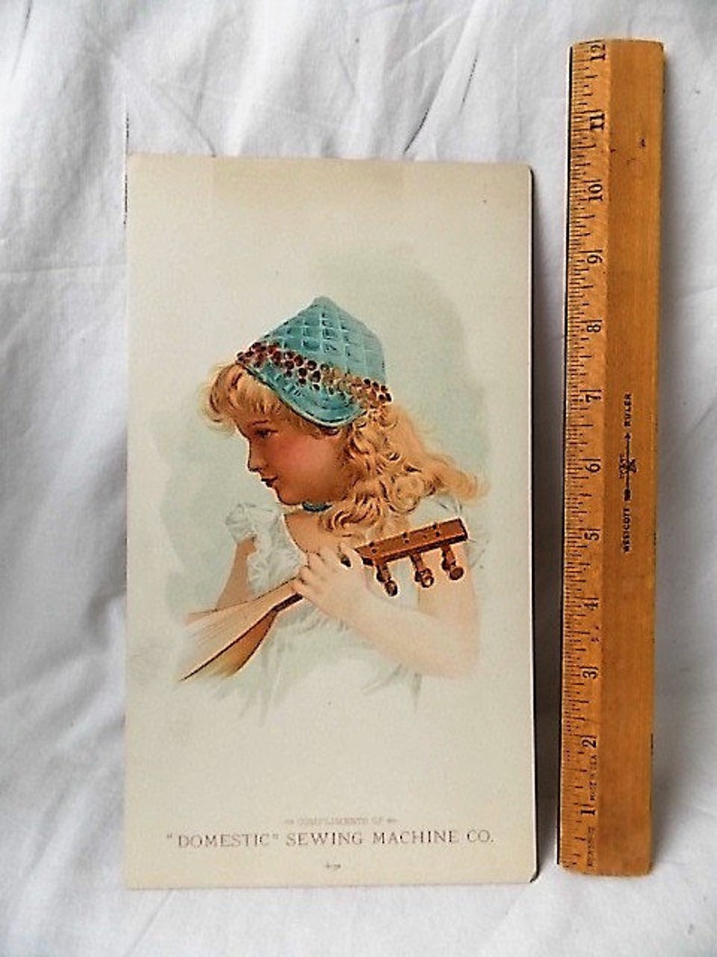 Może przedstawiać: Zabytkowa reklama drukowana dla "Domestic" Sewing Machine Co. przedstawiająca młodą dziewczynę z blond włosami w niebieskim berecie i trzymającą mały instrument strunowy. Drewniana linijka jest umieszczona po prawej stronie nadruku.