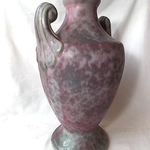 May include: A speckled, antique-style vase with a wide base and two curved handles. The vase has a pink and gray mottled pattern, with a light green rim and base. The overall shape is reminiscent of a classic urn.