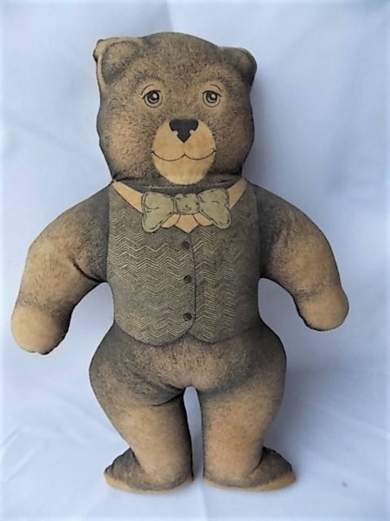 May include: A stuffed teddy bear with a light brown face, paws, and feet, and a darker brown body. The bear wears a vest with a herringbone pattern and a bow tie. The bear has button eyes and a stitched nose.