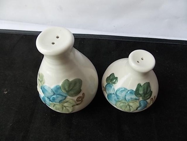 Peut inclure: Une paire de sali&egrave;res et poivri&egrave;res en c&eacute;ramique. Les sali&egrave;res blanches ont une forme arrondie et un petit dessus rond avec deux trous. Chacune est d&eacute;cor&eacute;e de motifs floraux bleus et verts.
