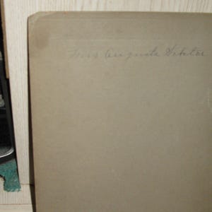 May include: A vintage photograph with the handwritten inscription "Mrs. Augusta Viktor" in cursive script. The photograph has a light brown color and is slightly worn, suggesting age. The corner of the photo is visible.