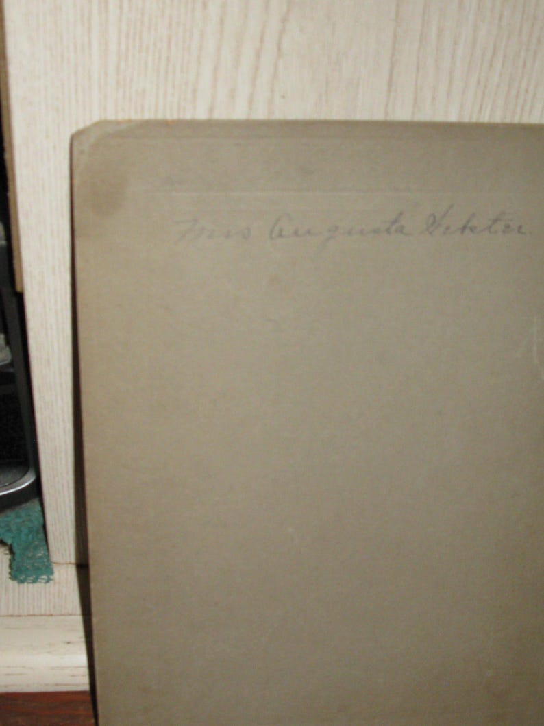 May include: A vintage photograph with the handwritten inscription "Mrs. Augusta Viktor" in cursive script. The photograph has a light brown color and is slightly worn, suggesting age. The corner of the photo is visible.