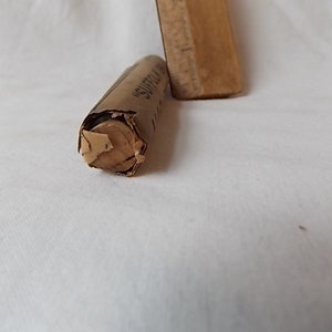 May include: A partially unwrapped, cylindrical object made of tan paper, with the word "SUFFOLK" visible. A wooden rectangular object is partially visible in the background. The objects are on a white surface.