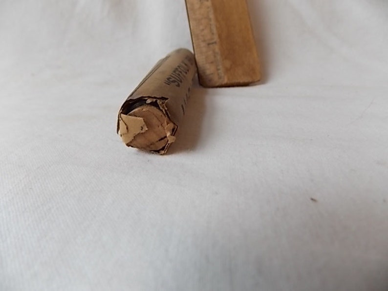 May include: A partially unwrapped, cylindrical object made of tan paper, with the word "SUFFOLK" visible. A wooden rectangular object is partially visible in the background. The objects are on a white surface.