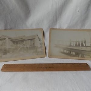 May include: Two vintage black and white photographs. One depicts a house with a porch, the other shows people on a pier. A wooden ruler rests below the photos.