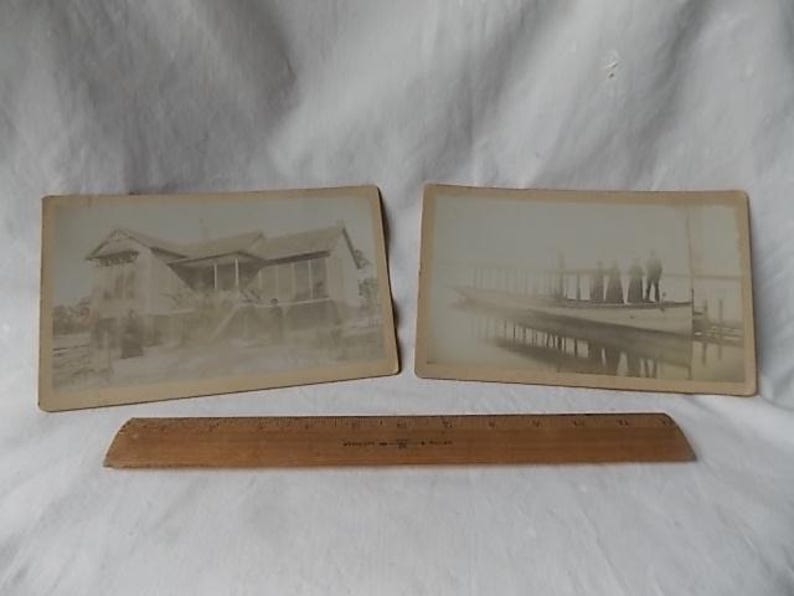 May include: Two vintage black and white photographs. One depicts a house with a porch, the other shows people on a pier. A wooden ruler rests below the photos.