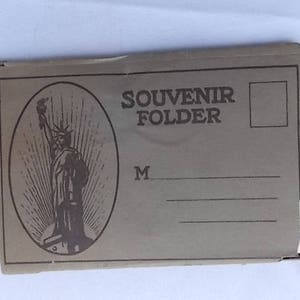 Może przedstawiać: Beżowa teczka pamiątkowa z ilustracją Statuy Wolności w owalnej ramce. Napis "SOUVENIR FOLDER" wydrukowany nad liniami do pisania. Teczka jest lekko zużyta.