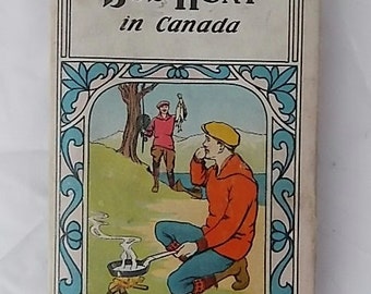 May include: A vintage hardcover book titled Bob Hunt in Canada by George W. Orton. The cover features a color illustration of two people outdoors, one cooking in a pan over a fire and another holding a fish, framed by blue decorative borders.