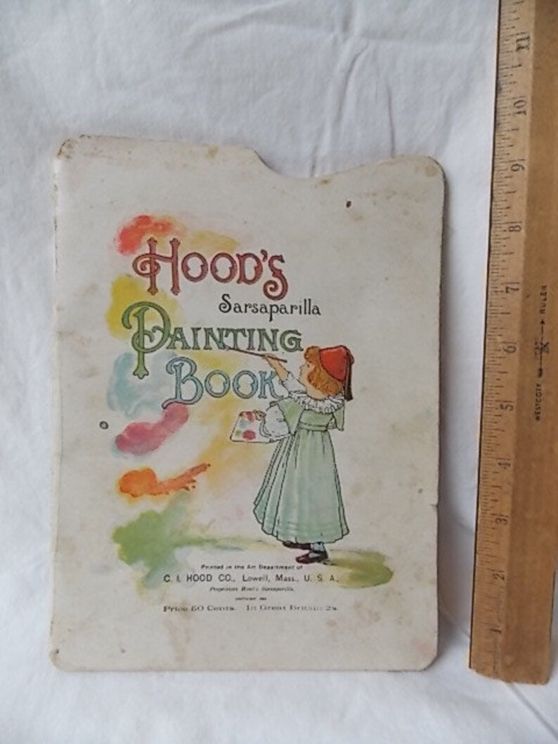 Puede incluir: Un libro de colorear vintage de Hood's Sarsaparilla con una cubierta clara que muestra a un ni&ntilde;o con un vestido verde sosteniendo un pincel y una paleta. Una regla de madera al lado muestra que el libro mide aproximadamente 28 cm de alto.