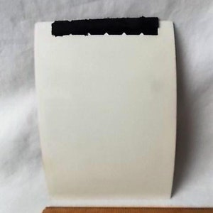 May include: A white, rectangular card with a black, textured strip across the top. A wooden ruler with inch markings is at the bottom of the image.