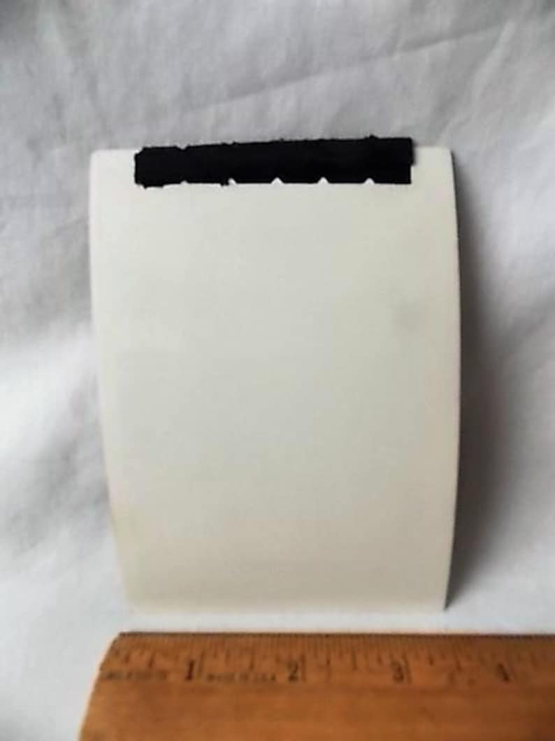 May include: A white, rectangular card with a black, textured strip across the top. A wooden ruler with inch markings is at the bottom of the image.