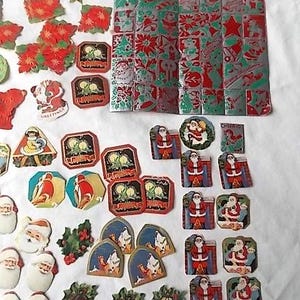 May include: A collection of vintage Christmas paper ephemera including die-cut Santa Claus figures, poinsettia shapes, gold stars, and a large rectangular sheet featuring a repeating grid of festive holiday motifs in red, green, and silver foil.
