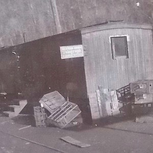 K&ouml;nnte beinhalten: Ein Schwarz-Wei&szlig;-Foto eines rechteckigen Geb&auml;udes mit der Aufschrift Western Union Telegraph & Cable Office. Das Bauwerk verf&uuml;gt &uuml;ber ein einzelnes Fenster, eine Treppe und mehrere Holzkisten, die an der Au&szlig;enwand gestapelt sind.